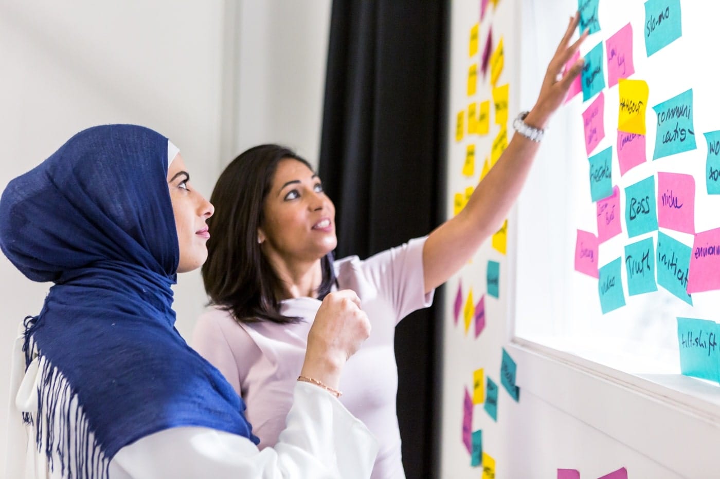 Women co-creating a post-it note vision wall, showcasing participatory design, shared power, and community-led planning.