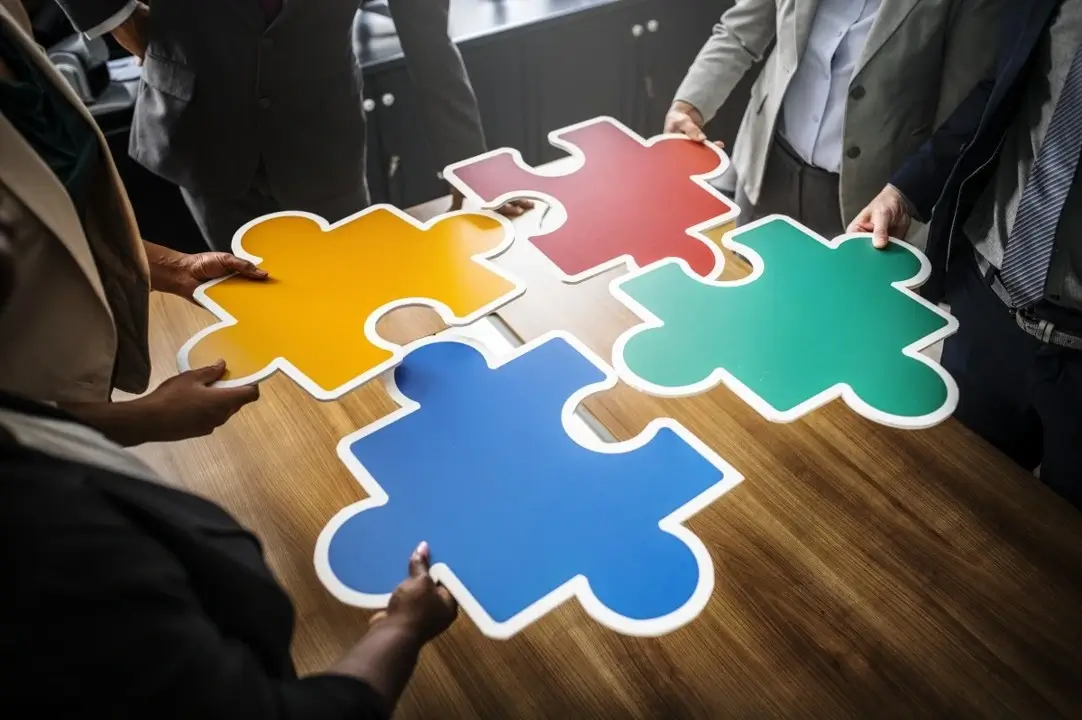 puzzle-pieces-team-work Multiple hands working together to connect colorful puzzle pieces, symbolizing collaboration and teamwork.