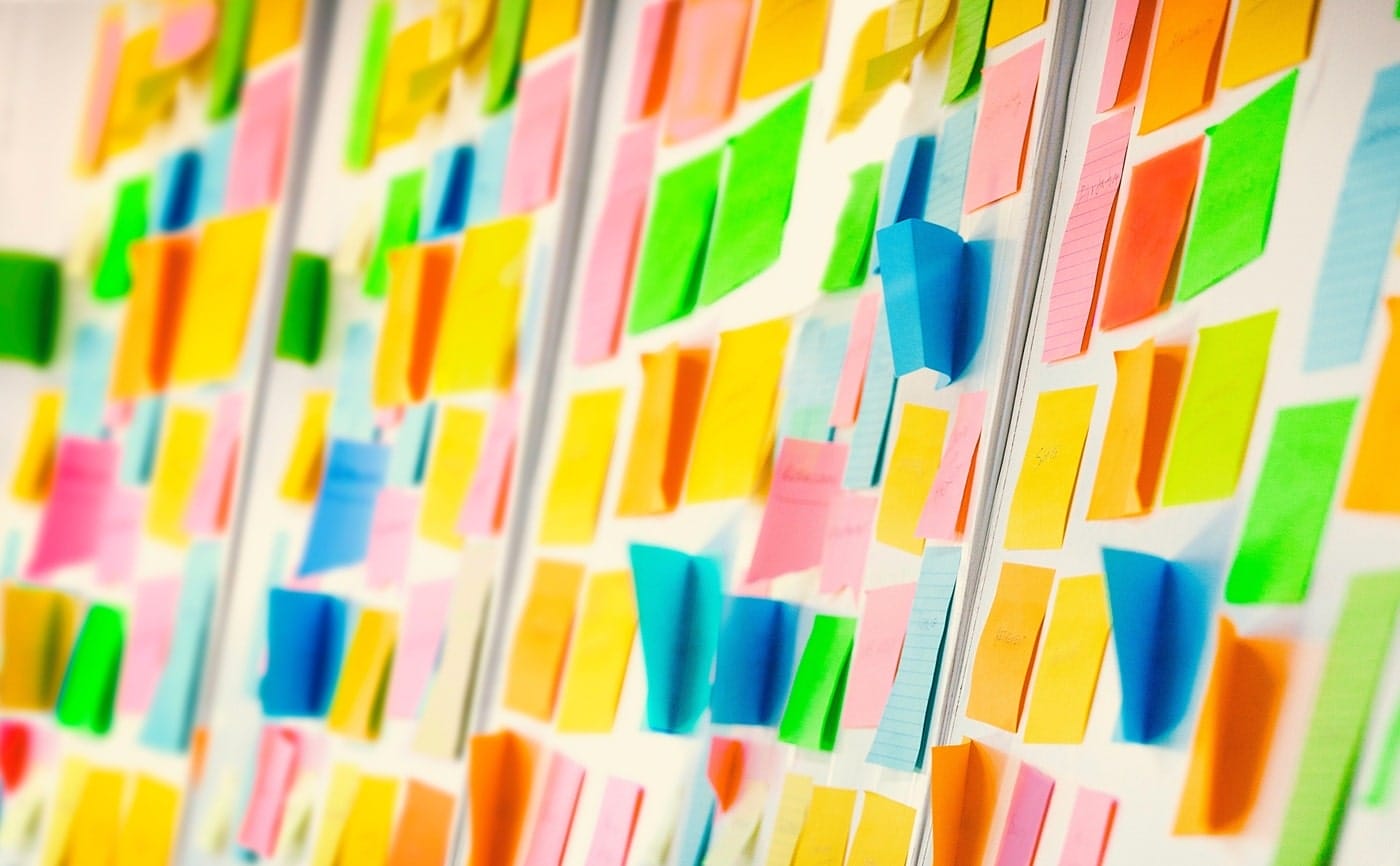 A wall covered with colorful sticky notes, each containing handwritten messages or reminders, arranged in a collage-like pattern.