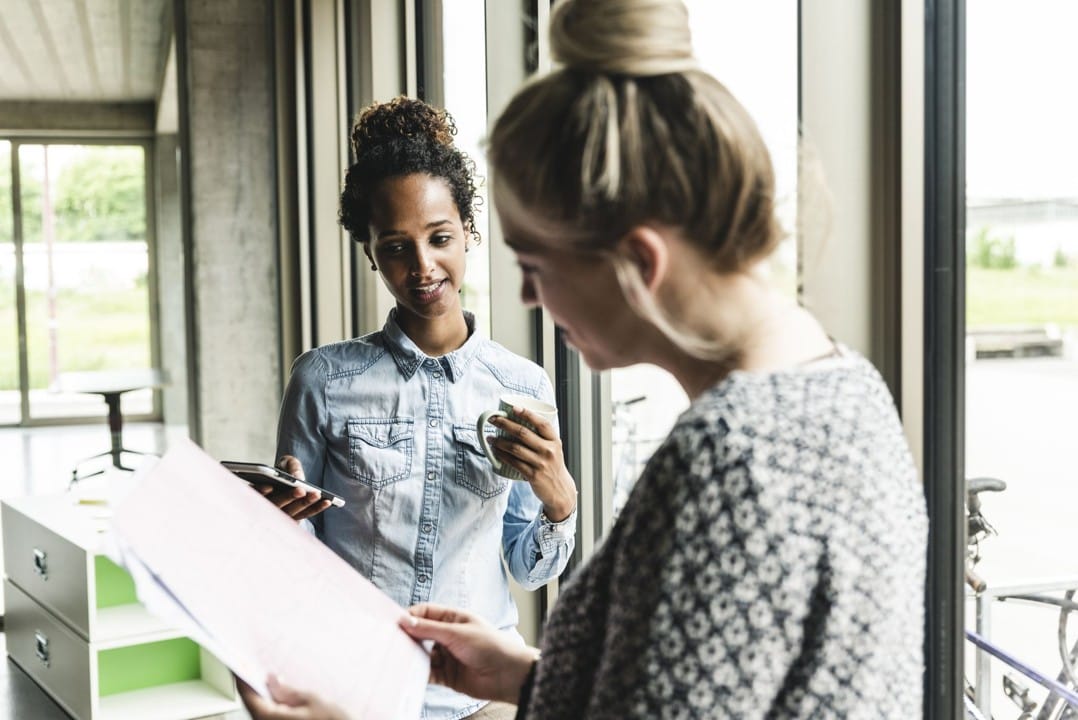 Two women collaborating on a document, reviewing feedback together—one pointing at the page while the other listens attentively.