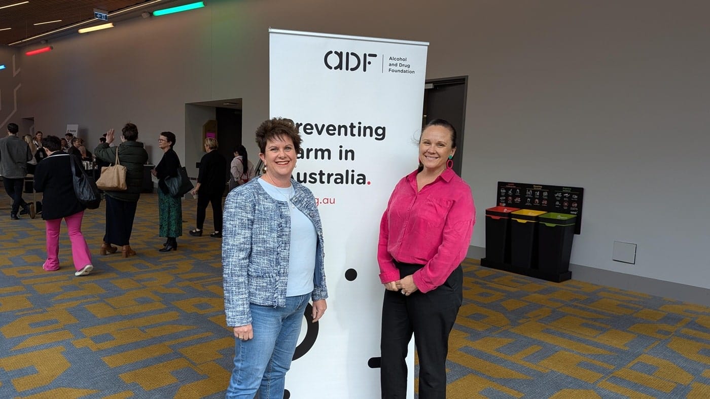 two-female-clinicians-at-adf-event-banner Two female clinicians posing at ADF event banner, showcasing partnership and user-centered health design.