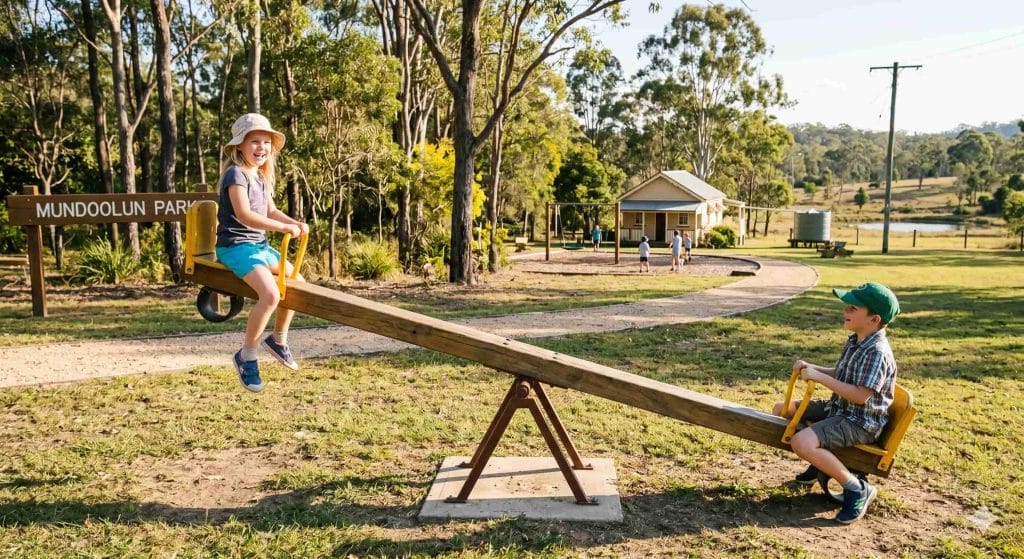 Children playing on see-saw in public park on sunshine day, representing joy, balance, and inclusive community spaces.